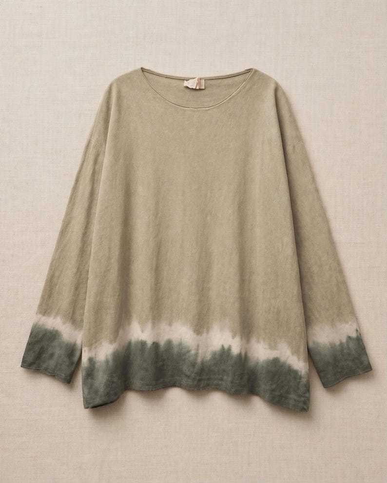 May include: A long-sleeve shirt in a muted sage green hue, featuring a round neckline and a dip-dye effect at the hem. The garment transitions from a light olive tone at the top to a darker forest green shade at the bottom with a white band.
