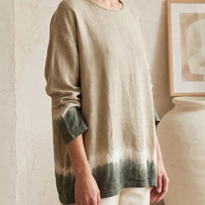 May include: A long-sleeve shirt featuring a round neckline and a relaxed fit. The garment displays a gradient color pattern, transitioning from a light beige at the top to a white band, and ending in a dark forest green at the hem and cuffs.