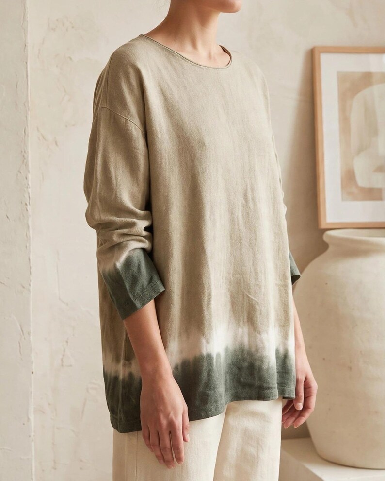 May include: A long-sleeve shirt featuring a round neckline and a relaxed fit. The garment displays a gradient color pattern, transitioning from a light beige at the top to a white band, and ending in a dark forest green at the hem and cuffs.