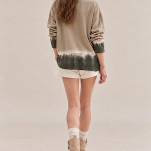 May include: A long-sleeve pullover sweater featuring a beige upper section that transitions into a dark green dip-dye hem, paired with off-white shorts, white ribbed crew socks, and beige mid-calf boots with side buckle strap details.