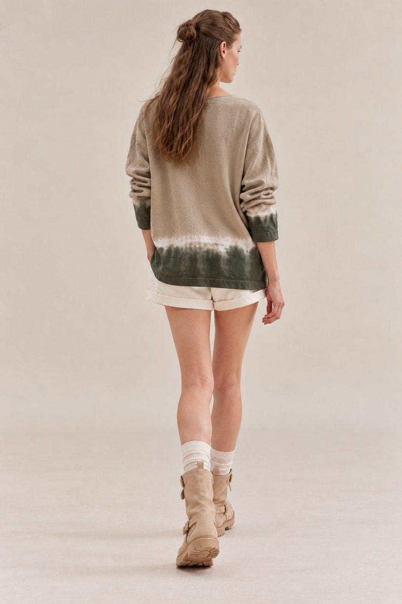 May include: A long-sleeve pullover sweater featuring a beige upper section that transitions into a dark green dip-dye hem, paired with off-white shorts, white ribbed crew socks, and beige mid-calf boots with side buckle strap details.