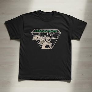 May include: Black t-shirt featuring a beige and green graphic of a vintage film camera inside a diamond shape. The word "PANAVISION" is printed in green above the camera. The shirt is made of a soft material.