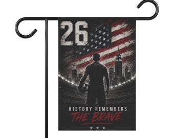 Op de afbeelding: Een rechthoekige tuinvlag met een voetballer die een bal vasthoudt, de skyline van New York City en een verweerde Amerikaanse vlag. Het getal 26 staat bovenaan, met de tekst HISTORY REMEMBERS THE BRAVE onderaan afgedrukt.