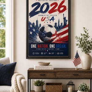 Puede incluir: Un p&oacute;ster enmarcado con el texto 2026 SUMMER OF SOCCER USA, UNITED BY PASSION y ONE NATION. ONE DREAM. El dise&ntilde;o incluye un bal&oacute;n de f&uacute;tbol con patrones de la bandera estadounidense, un horizonte urbano, la Estatua de la Libertad y colores rojo, blanco y azul.