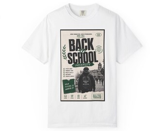 Op de afbeelding: Een wit t-shirt met korte mouwen en een rechthoekige grafische print met de tekst "BACK TO SCHOOL UNIVERSITY" en "NEW SEMESTER, NEW STANDARDS". Het ontwerp bevat een zwart-witafbeelding van een persoon met een rugzak en groene accenten.