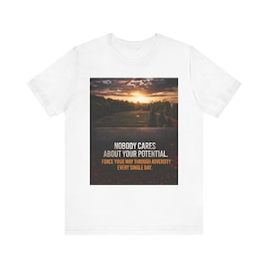 Puede incluir: Camiseta blanca con un gráfico de paisaje de puesta de sol y el texto "NOBODY CARES ABOUT YOUR POTENTIAL. FORCE YOUR WAY THROUGH ADVERSITY EVERY SINGLE DAY." El gráfico es rectangular.