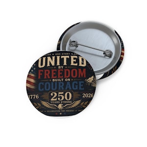 May include: A round button with a patriotic design. The button features the text "UNITED BY FREEDOM BUILT ON COURAGE" with the years 1776 and 2026. The button has a metal pin back and a distressed, vintage look.