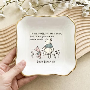 May include: A white ceramic trinket dish with a gold rim, featuring a Winnie the Pooh and Piglet illustration. The dish has the text "To the world, you are a mum, but to me, you are my whole world. Love Sarah xx."