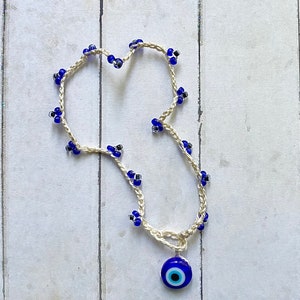 May include: A white crocheted anklet with blue evil eye beads and a blue evil eye charm.