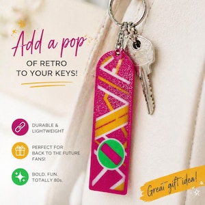 Puede incluir: Un llavero rectangular rosa y amarillo con un diseño de aeropatín, sujeto a un llavero con llaves. El llavero tiene el texto "Add a pop of retro to your keys!" y "Great gift idea!"