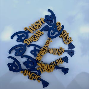May include: A collection of wooden key-shaped ornaments in navy blue and gold. Each key features a word such as "WISH", "DREAM", and "MAGIC". The keys have a decorative design.
