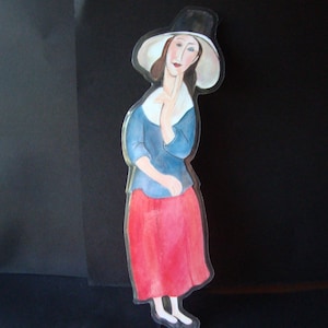 May include: A painted cutout of a woman in a blue top, red skirt, and a black hat with a white brim. The woman is depicted with a hand near her face, and white shoes. The cutout is against a black background.