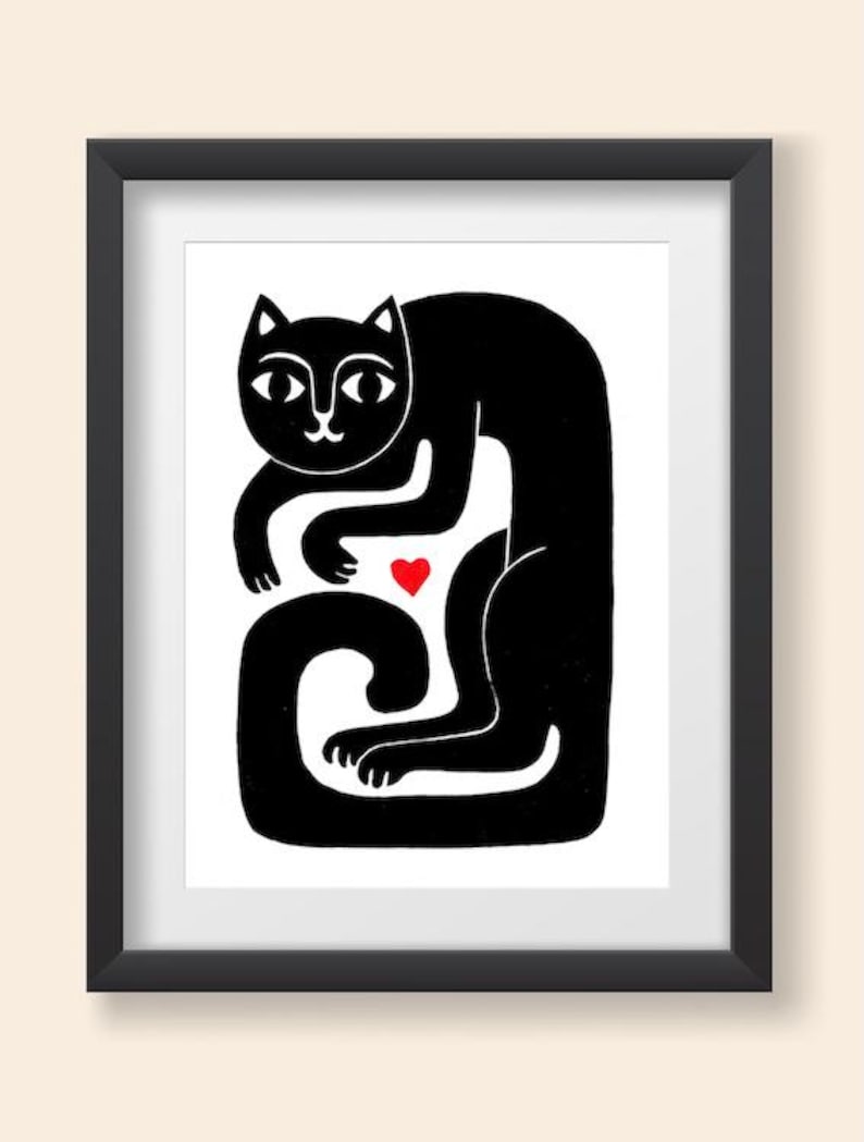 May include: A framed print featuring a stylized black cat illustration on a white background. The cat is depicted in a seated, curved posture with a small, solid red heart positioned between its front paws and its long, curled tail.