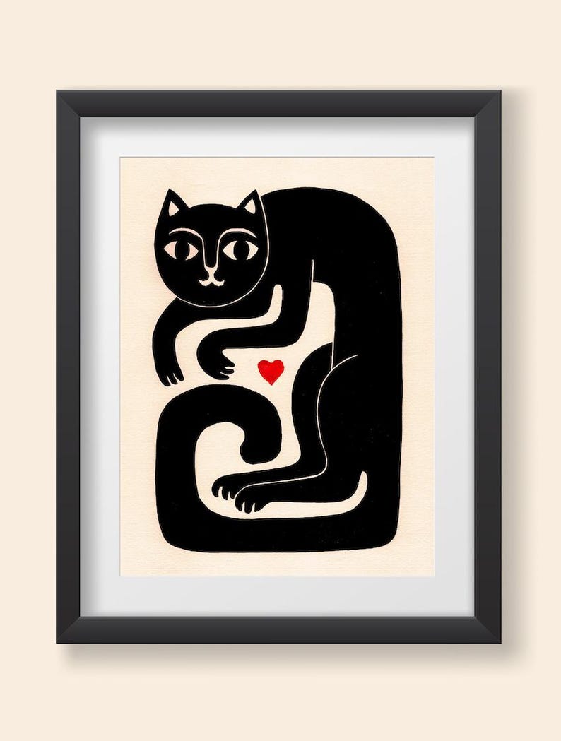May include: A framed print featuring a stylized black cat illustration on a cream background. The cat is depicted in a seated, curved posture with its long tail wrapped around its base. A small, solid red heart is positioned near the cat's chest.