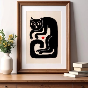 May include: A framed art print featuring a stylized black cat illustration on a cream background. The cat is depicted in a curled, seated position with a small, solid red heart centered between its front paws and its long, curved tail.