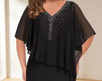 May include: A black dress featuring a V-neckline adorned with silver-toned rhinestones. The garment includes a sheer, layered cape-style overlay that drapes over the shoulders and chest, creating a flowing silhouette with short, wide sleeves.