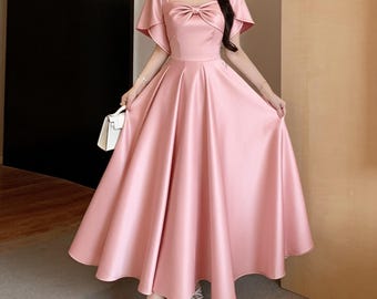 May include: A floor-length satin dress in a soft pink hue featuring a square neckline, short flutter sleeves, and a prominent bow detail at the center of the bodice. The skirt is full and flared, creating a voluminous silhouette with a smooth finish.