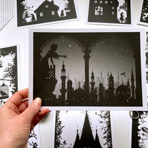 May include: A black and white silhouette print of a woman standing on a balcony overlooking a city skyline. The woman is reaching out with her hand, as if to touch the stars in the night sky. The city is filled with tall buildings and minarets, and the sky is filled with stars.