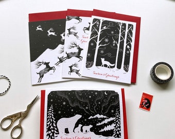 May include: A collection of holiday greeting cards with red envelopes. The cards feature black and white illustrations of reindeer, trees, a fox, and polar bears under a starry sky. The text "Season's Greetings" is printed in red.