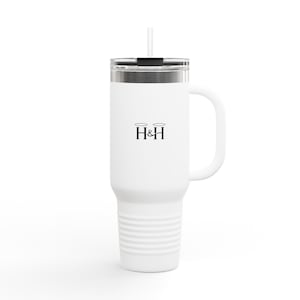 Puede incluir: Vaso térmico blanco con asa y pajita. El vaso tiene una tapa plateada y un cuerpo blanco con un logotipo negro de las letras "H&H" con halos encima. Diseñado para mantener las bebidas frías o calientes.