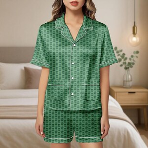 May include: Green pajama set with a heart pattern. The short-sleeved top has a notched collar, button-up front, and two front pockets. White piping trims the collar, cuffs, pockets, and shorts. The shorts have a matching heart pattern and white piping.