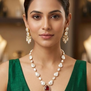 May include: A necklace featuring white baroque pearls and a central pendant with a red gemstone and a green enameled teardrop shape, finished with small pearl dangles. Matching drop earrings consist of a white pearl and a cluster of tiny pearls.