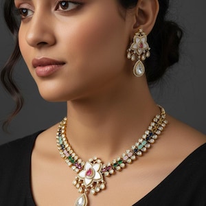 Peut inclure: Un ensemble collier et boucles d'oreilles dorés avec un motif floral orné de pierres précieuses colorées et de détails blancs. Le collier présente un grand pendentif avec une pierre en forme de goutte. Les boucles d'oreilles reprennent le design.