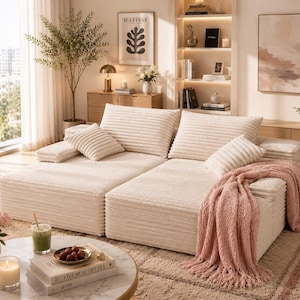 May include: A cream-colored corduroy sectional sofa with multiple cushions and a pink throw blanket. The sofa is in a well-lit living room with a coffee table, flowers, and artwork.