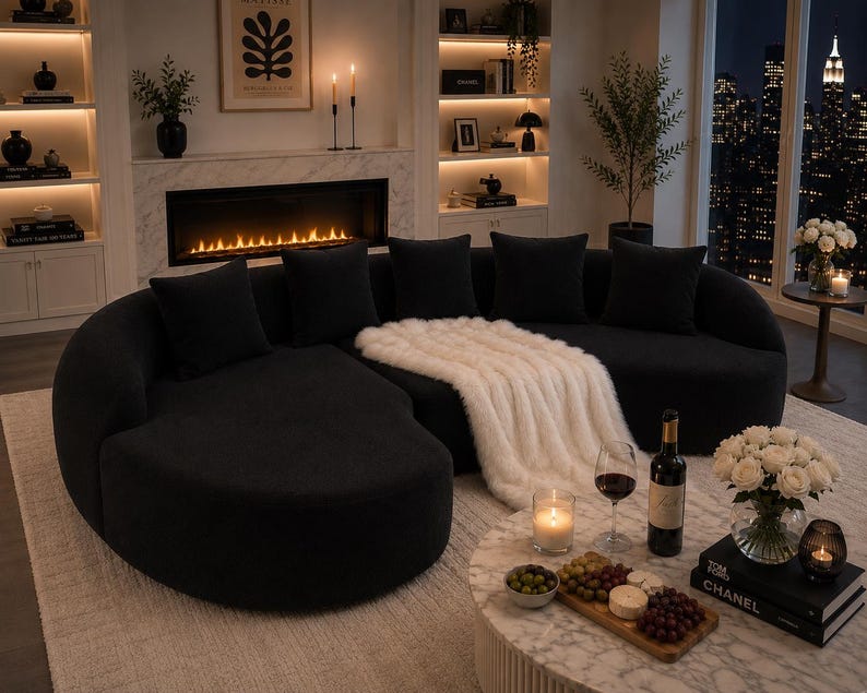 May include: A contemporary black sectional sofa with soft cushions and a curved shape. A white faux fur throw is draped over the sofa. A marble coffee table displays a wine bottle, glasses, and a candle.