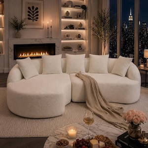 May include: An elegant living room with a large, cream-coloured sectional sofa and cushions. A marble coffee table displays a charcuterie board, wine, and a candle. A fireplace and city skyline view create a sophisticated, inviting atmosphere.