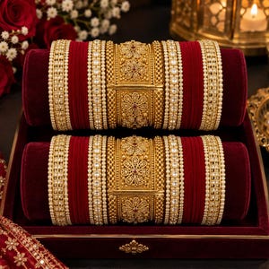 Puede incluir: Un conjunto de dos pilas de brazaletes a juego con bandas de terciopelo rojo intenso, piezas centrales de filigrana dorada con motivos florales y múltiples filas de pequeñas perlas blancas y cristales transparentes en un patrón estructurado.
