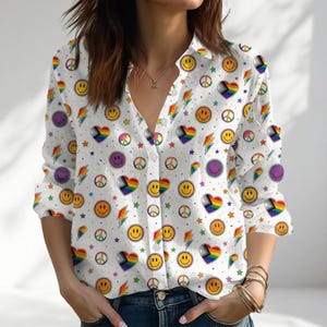 May include: A white long-sleeve button-down shirt featuring an all-over print of yellow smiley faces, multicolored peace signs, rainbow-colored hearts, lightning bolts, and small stars. The shirt has a classic collar and a front button closure.