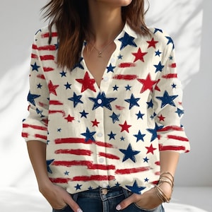 May include: Cream-colored button-down shirt with a patriotic star and stripe pattern. The long-sleeved shirt features red and blue stars and red brushstroke stripes. The shirt has a V-neck and is unbuttoned at the top.