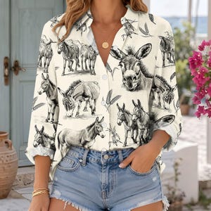 May include: A long-sleeve button-down shirt in an off-white color featuring a repeating black and white sketch-style print of donkeys and wheat stalks. The shirt has a classic collar, a front button placket, and long sleeves with cuffs.