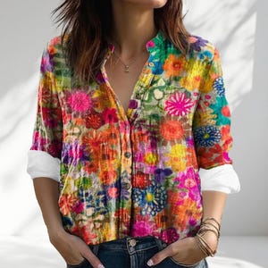 Pode incluir: Camisa com estampa floral vibrante em tons de rosa, amarelo, laranja e verde. Possui gola mandarim e botões. As mangas compridas têm punhos brancos. O decote está aberto.