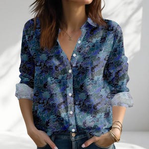 May include: A button-down shirt with a blue, black, and teal cloud pattern. The long-sleeved shirt has a classic collar and white buttons. The sleeves are rolled up, revealing a white cuff. The shirt is made of a lightweight fabric.