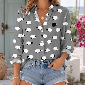 May include: A long-sleeve button-down shirt in a medium grey colour featuring an all-over print of small white sheep and one single black sheep with a red detail. The shirt has a classic collar, a front button placket, and long sleeves.