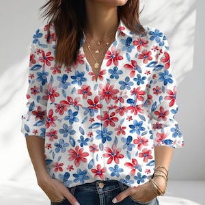 May include: White button-down shirt with a vibrant floral pattern. The shirt features a V-neck and long sleeves, adorned with red and blue flowers and green leaves. The floral print is spread across the entire shirt.