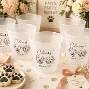 May include: A set of frosted plastic cups featuring a black line drawing of two dogs, the text "Cheers!" and "BELLA & COCO" printed on the front. The cups are arranged with a plate of paw-shaped cookies and a gift tag reading "THANK YOU FOR CELEBRATING WITH US!"