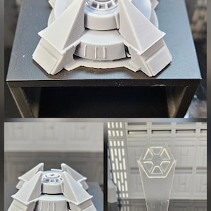 May include: A light gray 3D printed object featuring a circular base with four protruding triangular supports. One view shows a clear, flat, translucent vertical panel attached to the center, displaying a hexagonal emblem with six internal triangles.