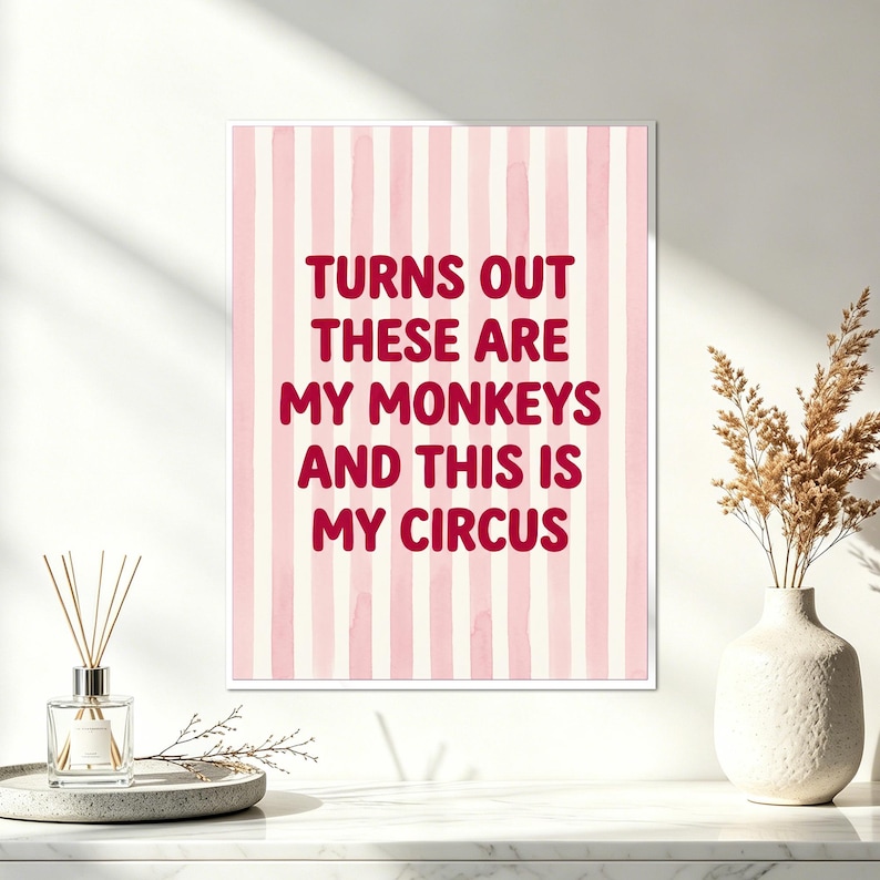 May include: A framed print with a pink and white striped background. The text in the center reads "TURNS OUT THESE ARE MY MONKEYS AND THIS IS MY CIRCUS" in a bold, red font. A decorative vase with dried flowers and a diffuser are in the foreground.