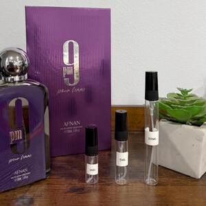 Puede incluir: Un juego de botella y caja de perfume morado con el texto "9 PM pour femme" y "AFNAN". El juego incluye tres viales de muestra y una peque&ntilde;a planta suculenta en una maceta de hormig&oacute;n. La botella mide unos 10 cm de alto.