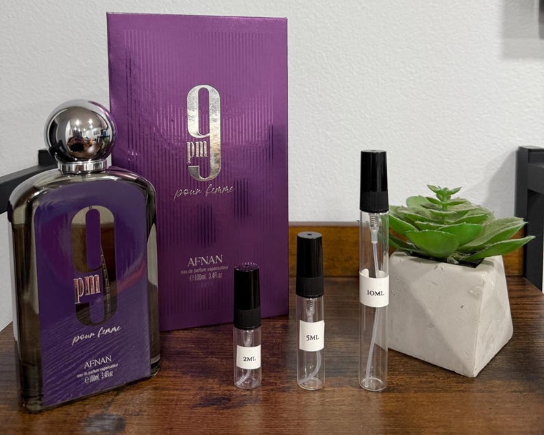 Puede incluir: Un juego de botella y caja de perfume morado con el texto "9 PM pour femme" y "AFNAN". El juego incluye tres viales de muestra y una peque&ntilde;a planta suculenta en una maceta de hormig&oacute;n. La botella mide unos 10 cm de alto.