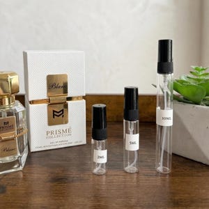 May include: A perfume set featuring a gold-capped glass bottle, a white box with gold accents, and several clear glass vials with black caps. The box reads "Prisme Collection Blanc". The vials are labeled 2ML, 5ML, and 10ML.