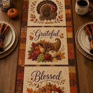 May include: A rectangular quilted table runner featuring four distinct panels with autumn themes. The panels display the words Thankful, Grateful, and Blessed, accompanied by illustrations of pumpkins, a turkey, a cornucopia, and fall leaves.