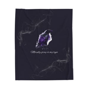 May include: A dark navy blue blanket featuring a stylized raven illustration in shades of purple and gray. Wispy white smoke-like designs surround the raven. The text "Morally gray is my type" is written in cursive below the raven.