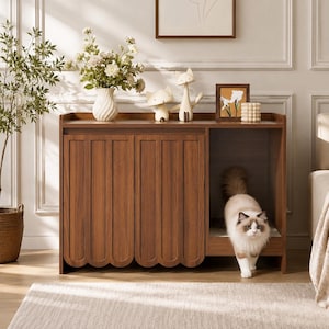 May include: A wooden cat litter box enclosure featuring two cabinet doors with a scalloped bottom edge design. The unit includes an open side compartment where a fluffy white and brown cat is stepping out. The top surface holds a white vase with flowers.