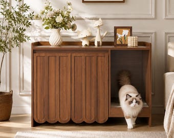 May include: A wooden cabinet with two doors featuring a scalloped bottom edge and a side compartment containing a fluffy white and brown cat. The top surface holds a white vase with flowers, two small fox figurines, a framed picture, and a textured object.