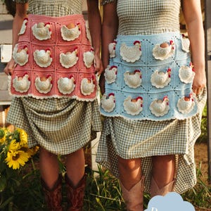 May include: Two crochet aprons, one pink and one blue, each adorned with white chicken appliqués and egg pockets. The aprons are worn over gingham dresses. The image also shows red and tan cowboy boots and sunflowers.