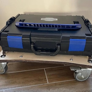 Peut inclure: Une boîte à outils industrielle noire avec des détails bleus et le mot "INDUSTRIAL" sur le couvercle. Elle est posée sur un chariot en bois avec quatre roulettes pour faciliter le déplacement.